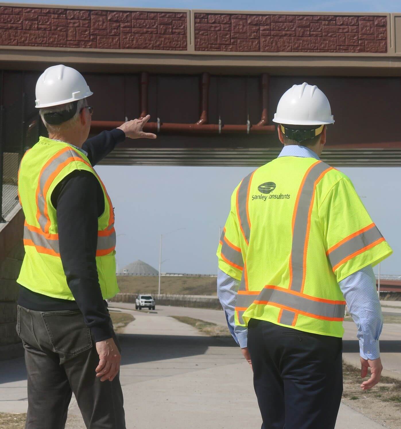 Two engineers in safety vests and hard hats, looking at a bridge