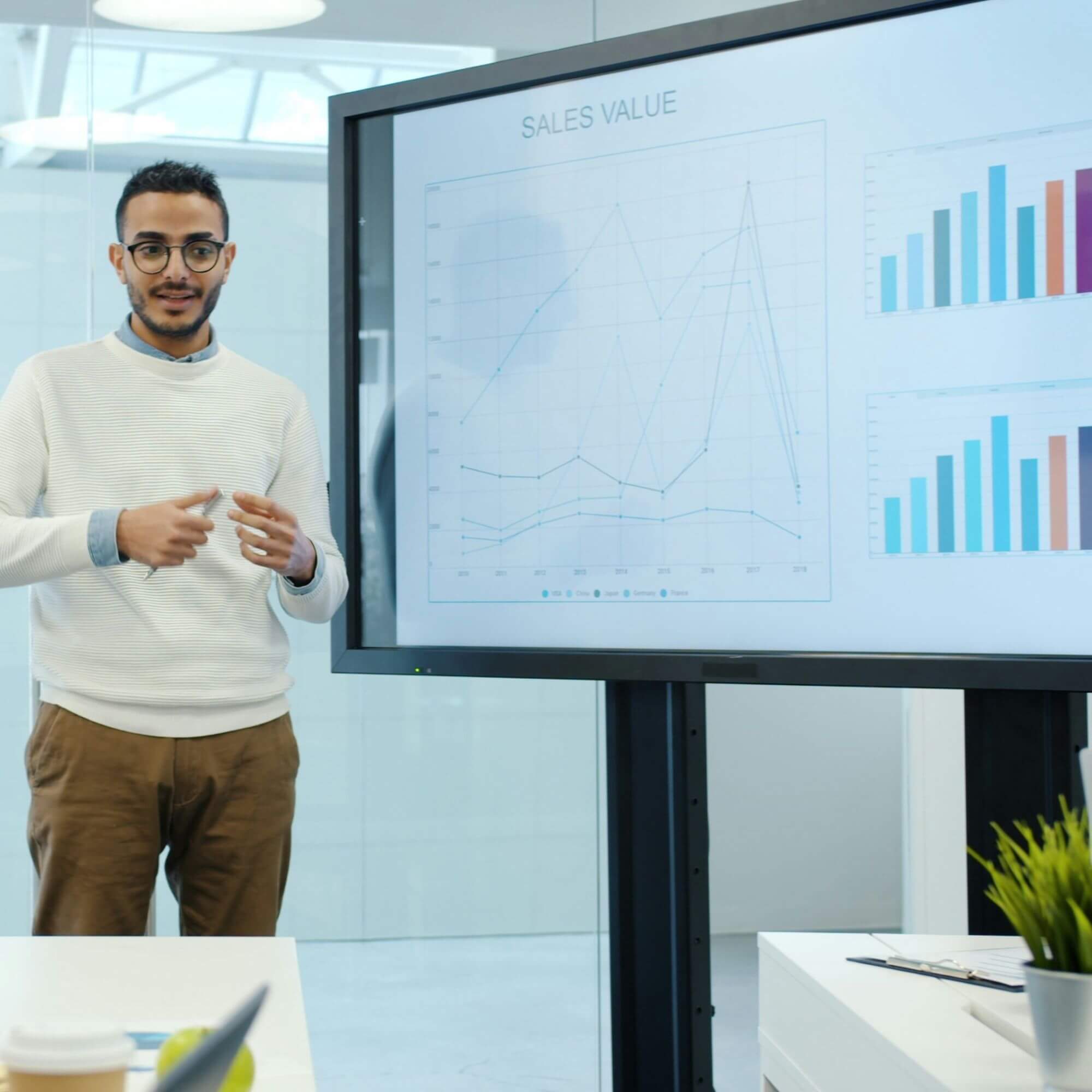 Professional presenting sales and performance charts on a digital screen during a team meeting, illustrating program monitoring, reporting and data analysis